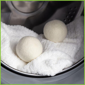 Two wool dryer balls sitting on a soft white towel inside a dryer.