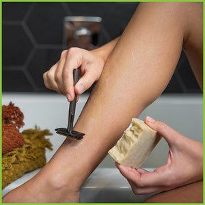 A woman shaving her leg using a slate grey safety razor and a bar of shaving soap.