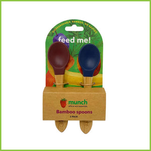 A pack of 2 soft silicone baby spoons. These feeding spoons are from the brand 'Munch', have bamboo handles and silicone tips in two different colours, purple and blue. The spoons are packaged in a simple cardboard holder.