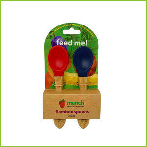 A pack of 2 soft silicone baby spoons. These feeding spoons are from the brand 'Munch', have bamboo handles and silicone tips in two different colours, red and blue. The spoons are packaged in a simple cardboard holder.