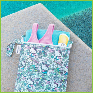 A licensed Hello Kitty wet bag laying next to a swimming pool. The bag is holding some togs, a towel and some suncream.