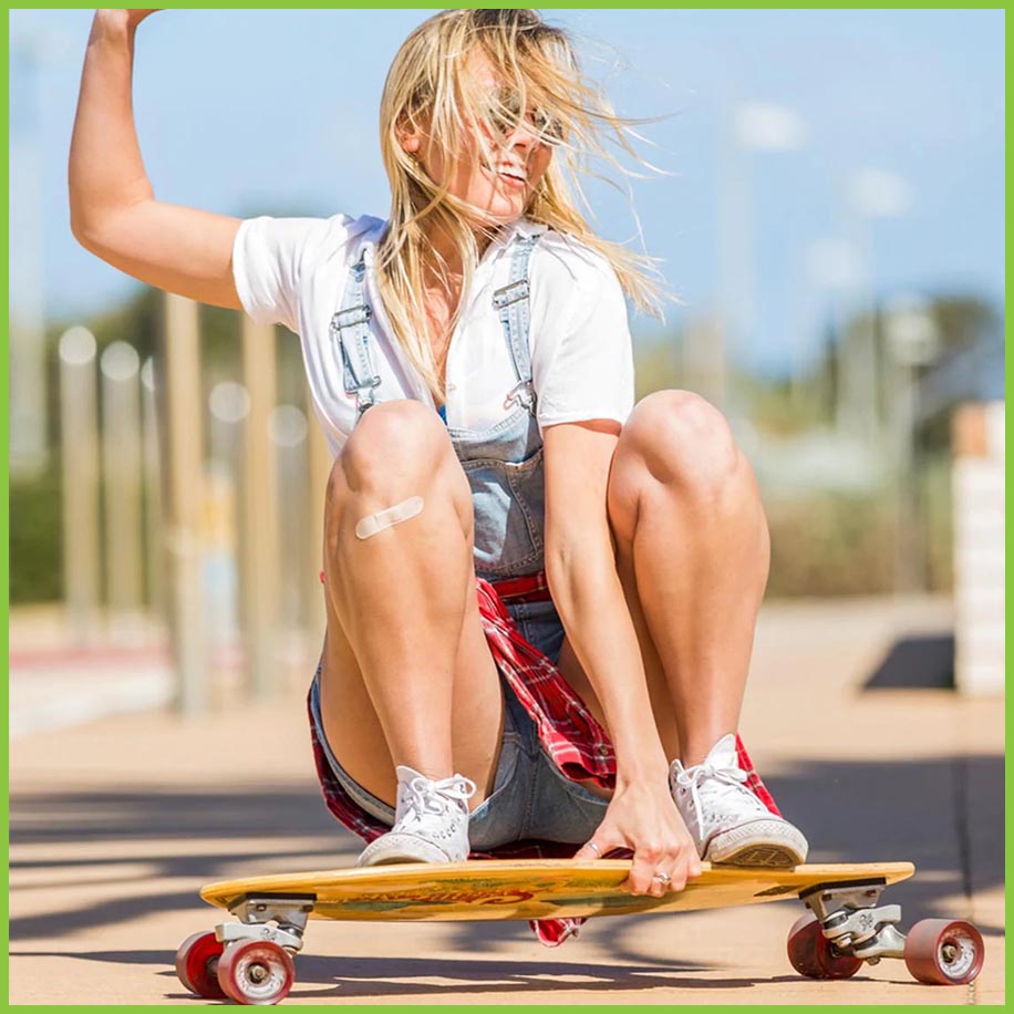 A woman skateboarding on a lovely summers day. She also has a PATCH plaster on her knee.