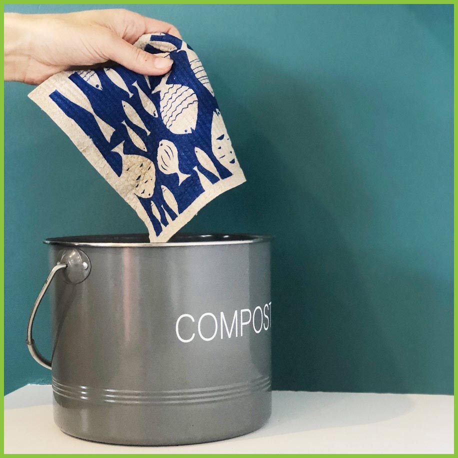 A Spruce Swedish dish cloth being held over a compost bin to demonstrate that they are 100% compostable at the end of their life.