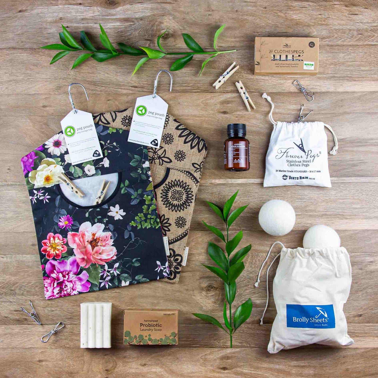A selection of eco friendly laundry products such a cotton peg bags, wool dryer balls, stainless steel pegs and bamboo pegs neatly laid out on a wooden floor.