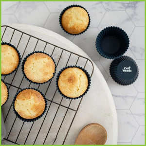 A cooling rack with freshly baked cupcakes cooling on the rack. The cupcakes are in reusable silicone muffin cases.