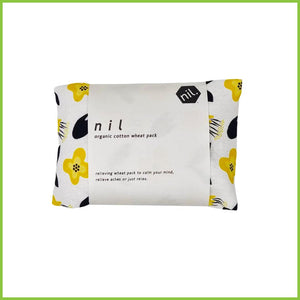A folded up wheat bag wrapped in a white packaging label. Label reads 'Nil organic cotton wheat pack. Relieving wheat pack to calm your mind, relieve aches or just relax.' This wheat bag has a bold yellow and black flower print.