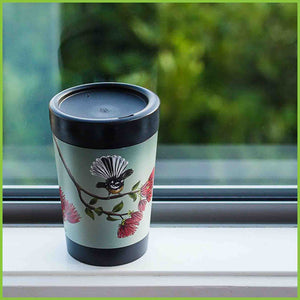A reusable cup by CuppaCoffeeCup with the Pohutukawa Fantail design sitting on a windowsill.
