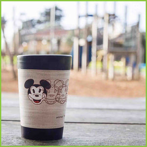A reusable cup by CuppaCoffeeCup with the Mickey to Tiki design sitting on a bench at a playground.