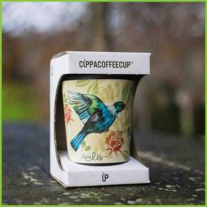 A reusable cup by CuppaCoffeeCup with the Tui design sitting on a park bench.