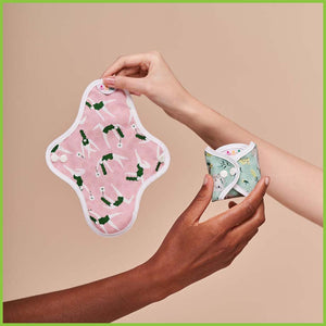 Two small sized sanitary pads being held up for the photo. One is showing the pattern side. The other is folded and fastened into a small neat square for storage.
