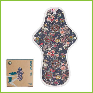 A large or overnight sized reusable sanitary pad from Hannah. The image shows the pad flat on a white background next to its packing box. The pattern on this pad is a dark grey covered with very pretty small flowers in varying shades of whites and pinks. This pattern is known as 'Antique Indigo'.