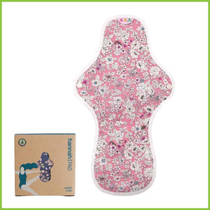 A large or overnight sized reusable sanitary pad from Hannah. The image shows the pad flat on a white background next to its packing box. The pattern on this pad is pink covered in small pretty white flowers. This pattern is known as 'Antique Pink'.