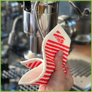 A Spruce Swedish dish cloth with the red stripe design being used to clean a coffee machine. The image is a close up so that the thickness and texture of the cloth can easily be seen.