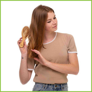Bamboo and natural rubber hair brush being used by a young woman to brush her hair. Side view.