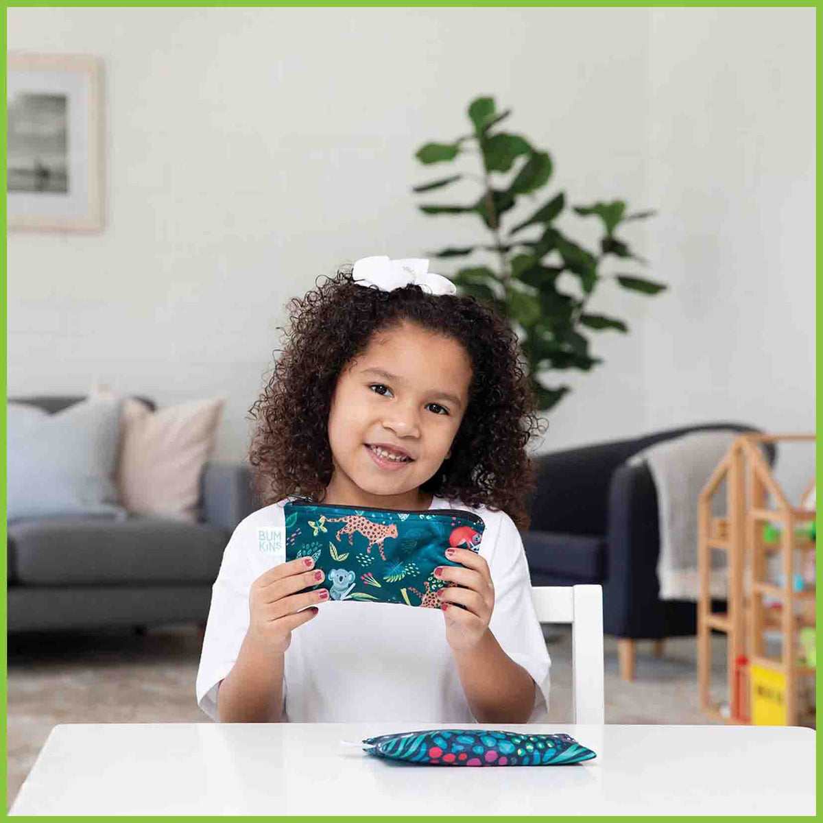 A young girl holding up a Bumkins snack bag with the jungle Animals design on it.