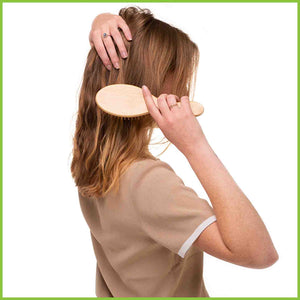 Bamboo and natural rubber hair brush being used by a young woman to brush her hair. Rear view.
