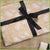A gift wrapped item with brown paper wrapping and a black cotton ribbon.