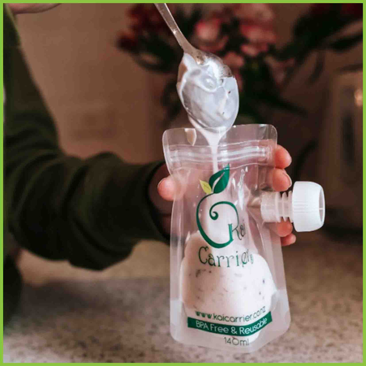 Someone filling a Kai Carrier food pouch using a spoon.
