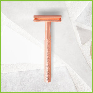 A copper safety razor lying on a grey surface.