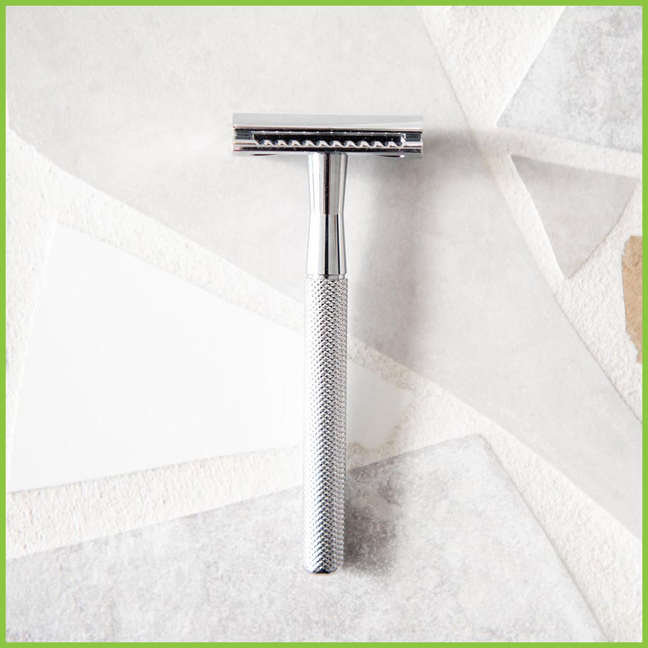 A silver stainless steel safety razor lying on a grey surface.