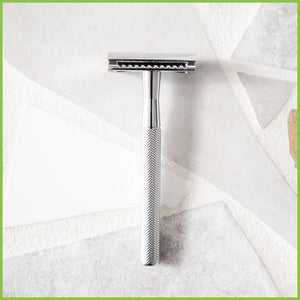 A silver stainless steel safety razor lying on a grey surface.