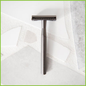 A slate grey coloured stainless steel safety razor lying on a grey surface.