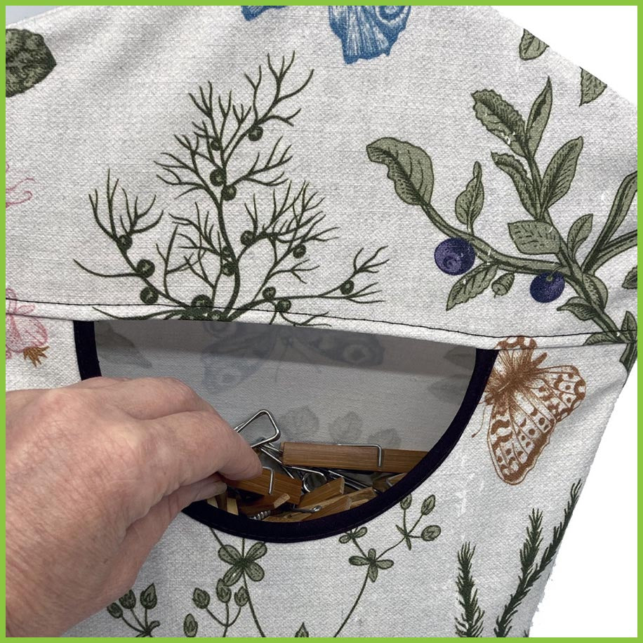 A close up of the opening of the peg bag. You can see pegs inside the peg bag as someone is reaching in to grab a peg.