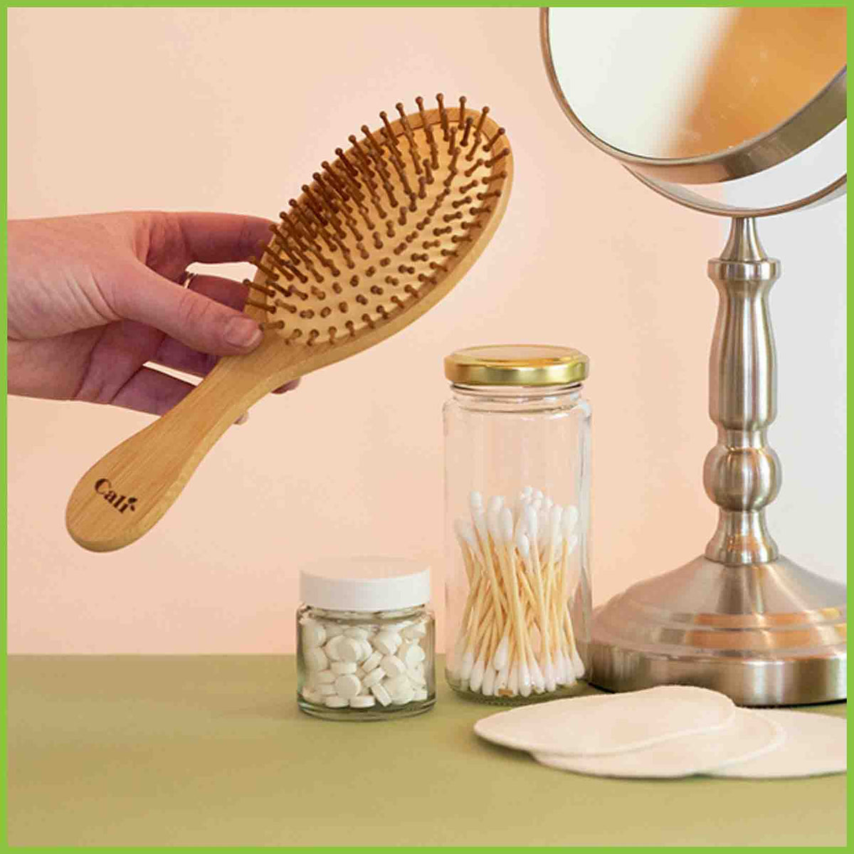 Bamboo and natural rubber hair brush being held next to other eco-products such as cotton buds, dental tabs and cotton facial rounds.