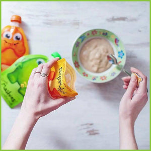 A women filling a Little Mahies reusable food pouch with baby food. She's holding a pouch in her left hand, and using her right hand to scoop food out of a bowl with a spoon, to then spoon it into the pouch, which is open from the bottom.