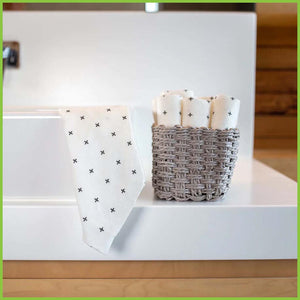 Reusable bamboo towels have been individually rolled and placed in to a small wicker basket next to a bathroom sink. One towel has been draped over the sink.
