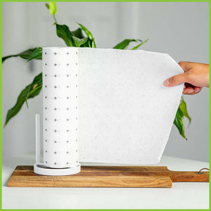 A roll of reusable bamboo towels standing on a wooden chopping board. A person is holding a sheet of towel out, almost ready to pull it off the roll.