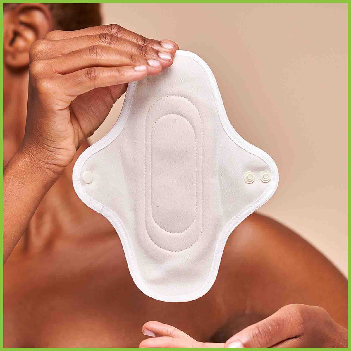 A small reusable sanitary pad from Hannah being held up by a woman. The organic cotton side of the pad is in full view allowing you to see the dome fasteners and the stitching pattern.