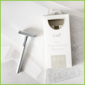 A silver safety razor lying on a grey surface next to its Caliwoods branded packaging.