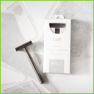 A slate grey safety razor lying on a grey surface next to its CaliWoods branded packaging.