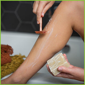 A woman shaving her leg using a copper safety razor and a bar of shaving soap.