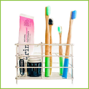 A wired stainless steel toothbrush holder with bamboo tootthbrushes, toothpaste and floss standing in it.