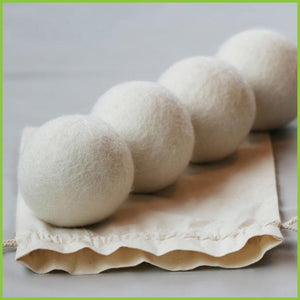 Four wool dryer balls in a line, sitting on top of a cotton storage bag.